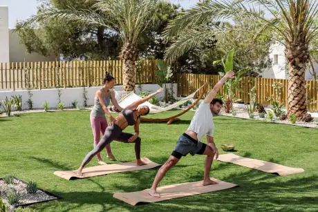 Sesión de práctica de yoga en 7Pines Resort Ibiza, con instructores y participantes en un entorno exterior sereno.