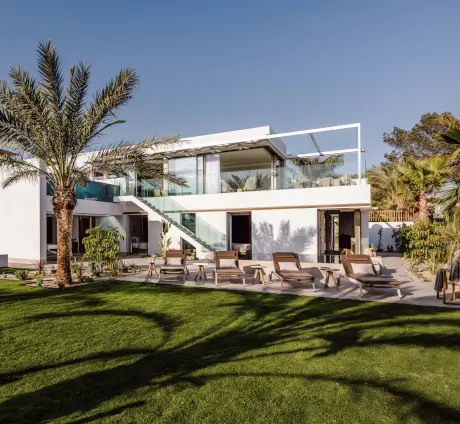 Modern villa with garden and lounge chairs on the cliffs of Ibiza.