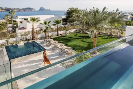 Mujer disfrutando de la vista de la piscina en 7Pines Resort Ibiza, cerca de palmeras y la costa de Ibiza.