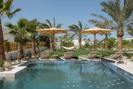Área de piscina relajante en 7Pines Resort Ibiza con tumbonas y palmeras.